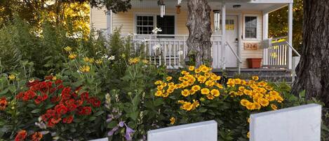 A house with a porch, a tree, and a variety of flowers in the foreground.