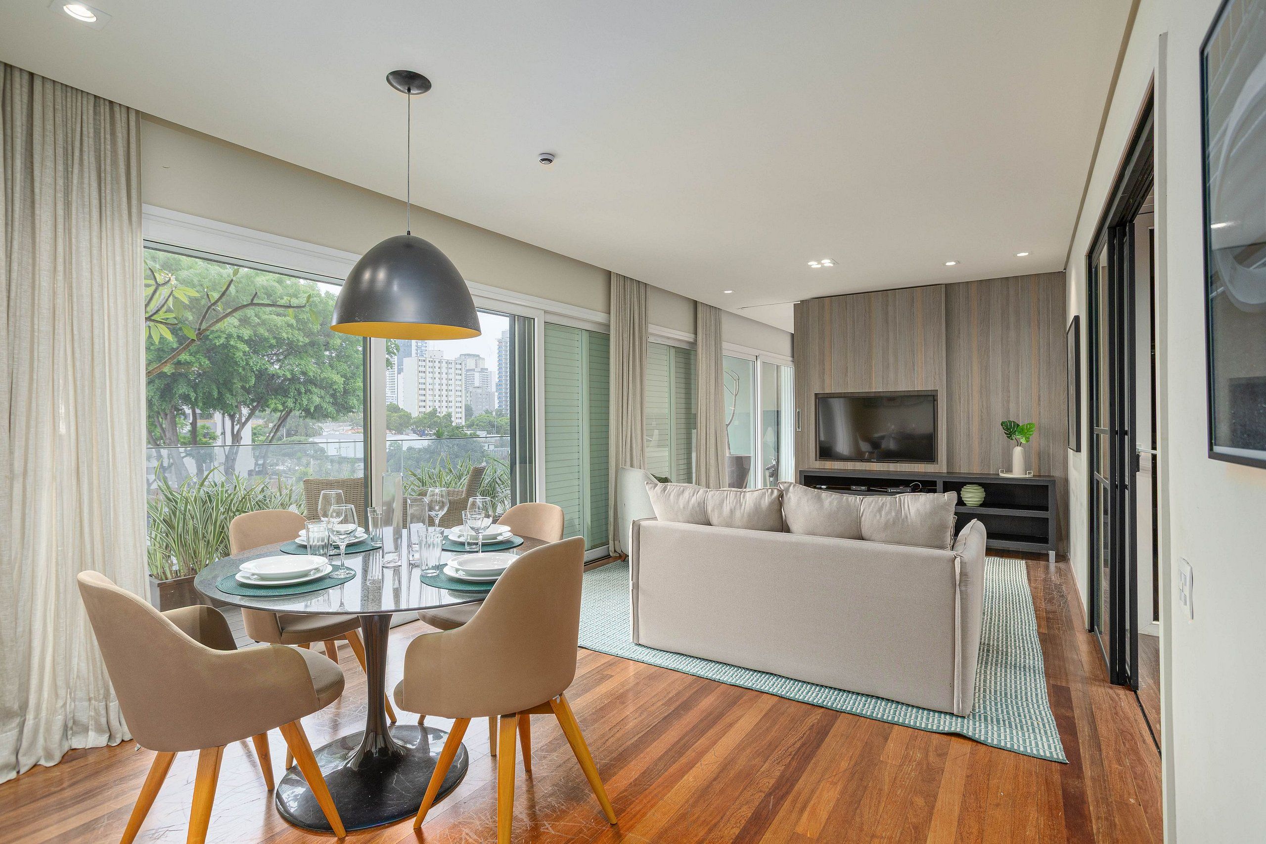 A modern living room with a dining area, large windows, and a flat-screen TV.