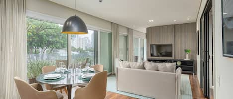 A modern living room with a dining area, large windows, and a flat-screen TV.