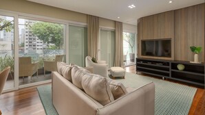 Una sala moderna con sofá, sillones, televisor y balcón con plantas.