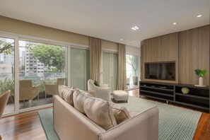 Un salon moderne avec un canapé, des fauteuils, un téléviseur et un balcon agrémenté de plantes.
