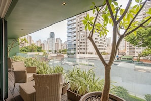 A balcony with wicker furniture, potted plants, and a view of a cityscape with high-rise buildings. - Edifício Triplo (São Paulo)