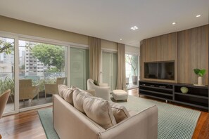A modern living room with a sofa, chairs, a TV, and a balcony with plants. - Edifício Triplo (São Paulo)