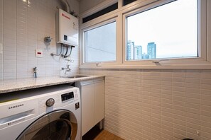 Une buanderie équipée d’un lave-linge Samsung, d’un chauffe-eau Rinnai et d’une fenêtre donnant sur la ville.