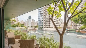 Un balcón con mobiliario de mimbre, plantas en macetas y vistas a un paisaje urbano con rascacielos.