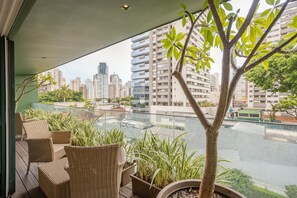 Un balcon agrémenté de meubles en osier, de plantes en pot et offrant une vue sur un paysage urbain avec de hauts immeubles.