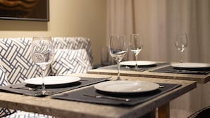 A dining table set with plates, cutlery, and wine glasses, with a patterned cushion in the background. - Edifício Triplo (São Paulo)