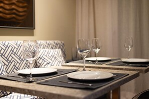 Une table à manger dressée avec des assiettes, des couverts et des verres à vin, et un coussin à motifs en arrière-plan.