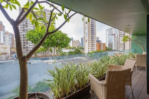 A balcony with wicker furniture, potted plants, and a view of a cityscape and river.
