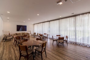 Une pièce spacieuse avec une grande table à manger entourée de chaises, d’un canapé et d’une grande fenêtre agrémentée de rideaux.