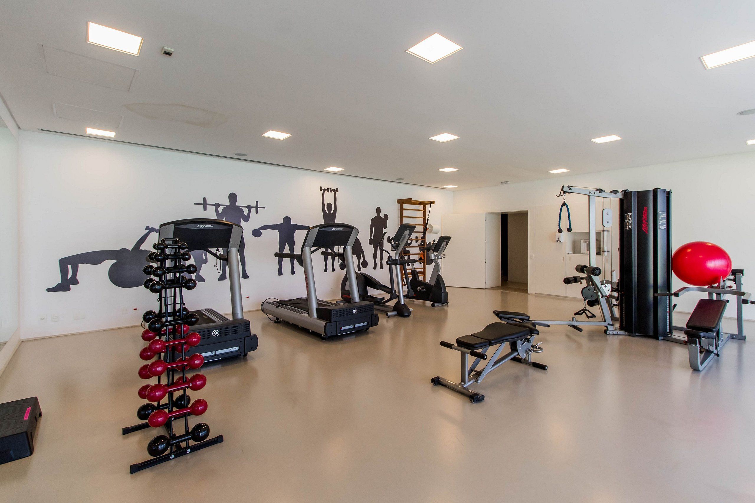 A gym with treadmills, weight machines, and a red exercise ball.