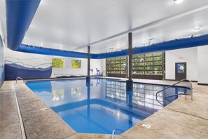 An indoor swimming pool with clear blue water, a mural on the wall, and a view of trees through large windows.