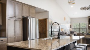Een moderne keuken met granieten aanrechtbladen, roestvrijstalen apparatuur en een groot kookeiland met barkrukken.
