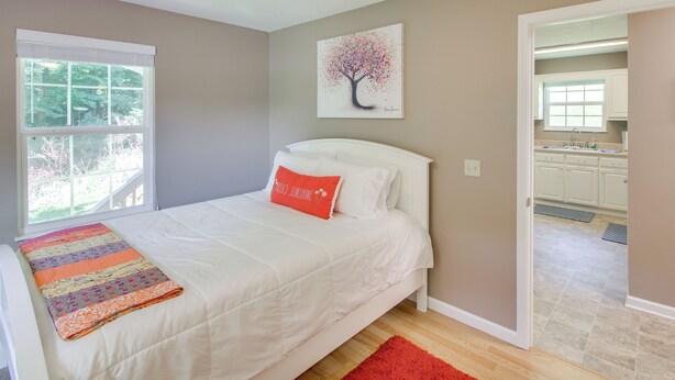 Une chambre à coucher avec un lit, une fenêtre, un ventilateur de plafond, un tableau et une vue sur la cuisine.