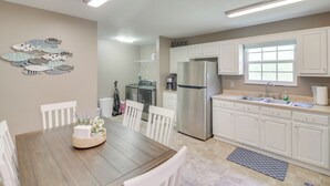 Une cuisine moderne avec des meubles blancs, un réfrigérateur en acier inoxydable et un coin repas comprenant une table en bois et des chaises blanches.