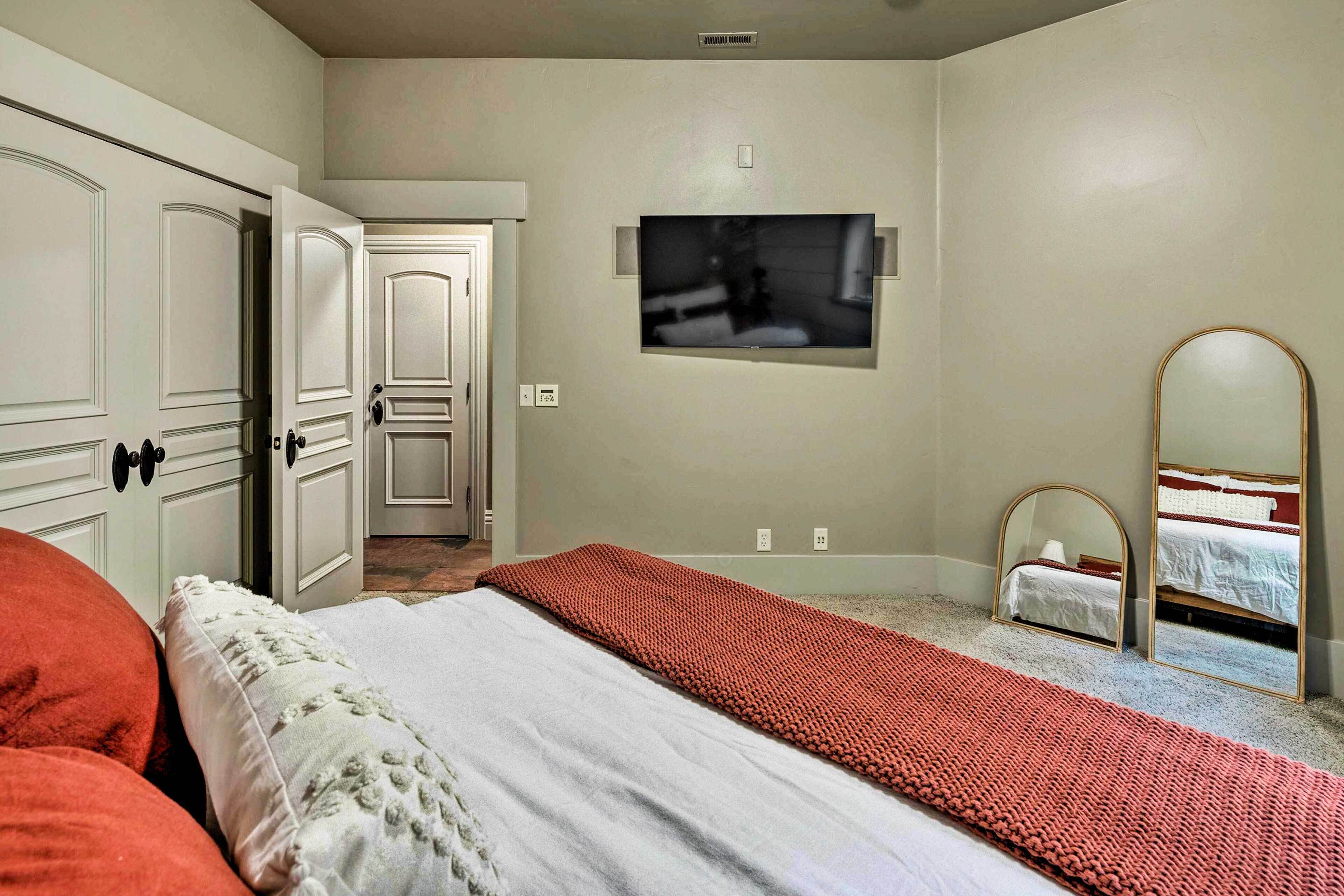 A bedroom with a bed, a TV, a mirror, and a door leading to another room.