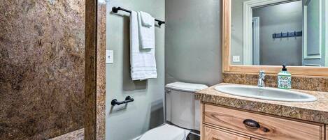 A bathroom with a marble shower, a toilet, a sink with a wooden vanity, and a mirror.