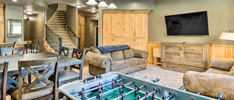 A spacious living room with a foosball table, a sofa, a coffee table, and a TV mounted on the wall.