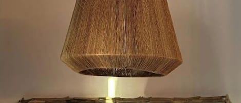 A pendant lamp with a woven shade hanging above a rustic sign that reads "BEACHHOUSE".