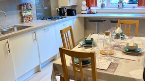 A modern kitchen with white cabinets, a gas stove, and a dining area set for four with wooden chairs and a table set with plates, bowls, and glasses. - Apartment Sleeps 5 With Free Parking (Edinburgh)