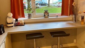 A kitchen with a window, a coffee machine, a plant, and two bar stools. - Apartment Sleeps 5 With Free Parking (Edinburgh)