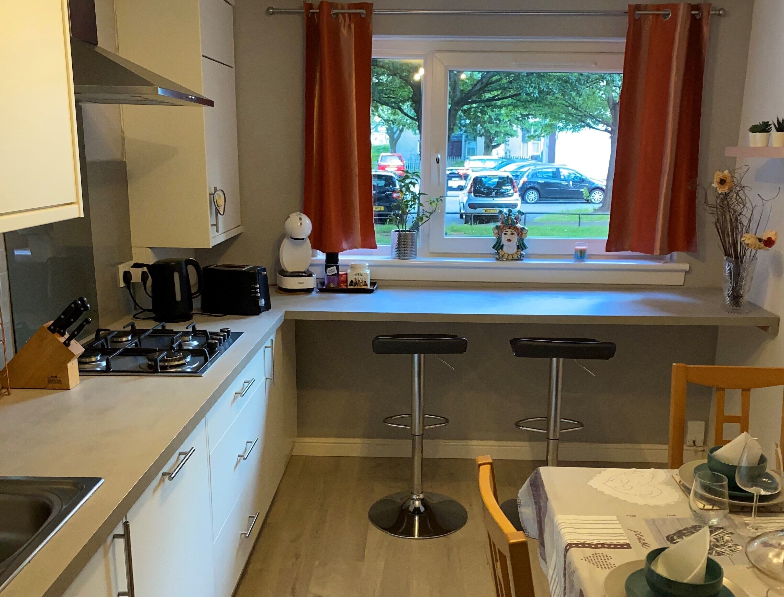 A modern kitchen with a gas stove, a coffee maker, and a window with curtains.
