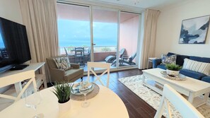 Una sala de estar con televisor, sofá, mesa baja y mesa de comedor con planta y copa de vino.