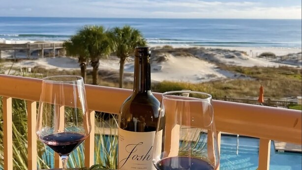A balcony with a view of the ocean, a bottle of wine, and two glasses on a railing.