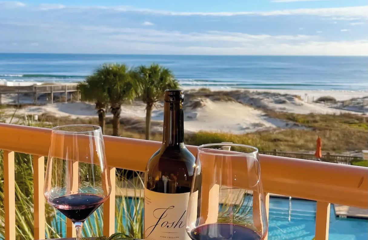 A balcony with a view of the ocean, a bottle of wine, and two glasses on a railing.
