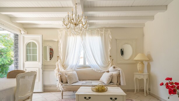 A room with a white sofa, a white table, a chandelier, a lamp, and a vase with red flowers. - Romantic house (Le Château-d'Oléron)