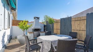 A patio with a round table and wicker chairs, a barbecue grill, and a wooden fence. - Romantic house (Le Château-d'Oléron)