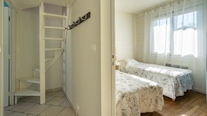 A bedroom with two beds, a staircase, and a window with sheer curtains. - Romantic house (Le Château-d'Oléron)