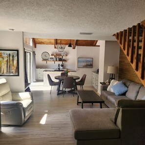 Uma sala de estar moderna com sofá, puf e área de jantar com cadeiras e mesa.