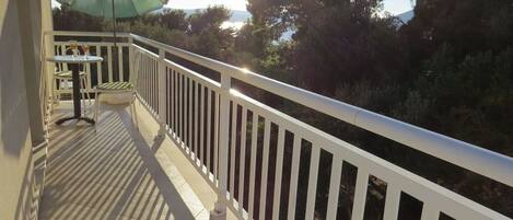 A balcony with a white railing, a table with two chairs, and a green umbrella.
