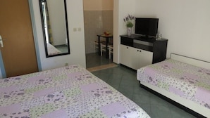 A hotel room with two beds, a desk with a television, and a small dining area.