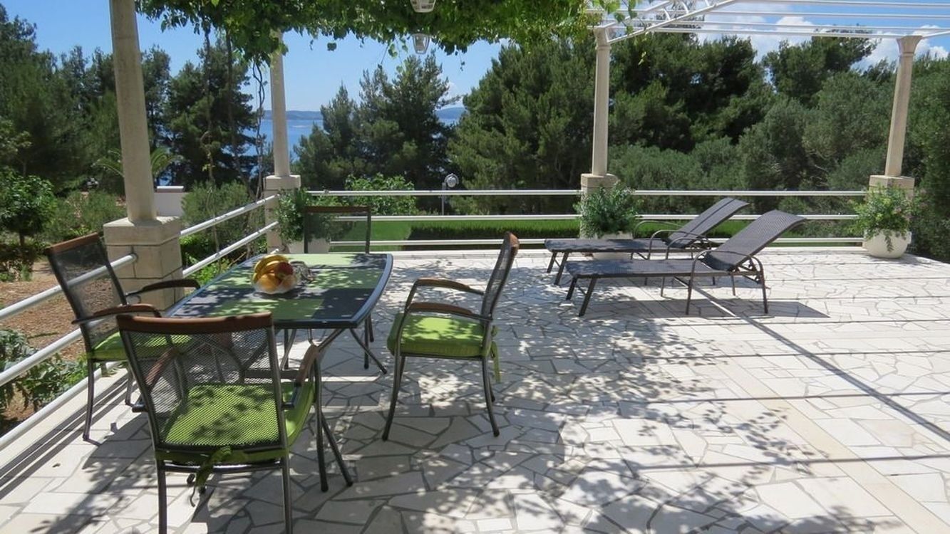 An outdoor patio with a table and chairs, a pergola, and a view of the sea.