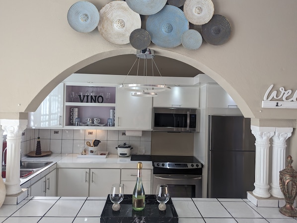 Una cocina moderna con muebles blancos, un letrero VINO, electrodomésticos de acero inoxidable y una encimera de mármol.