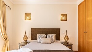 A neatly made bed with a brown headboard, two bedside lamps, and a stack of white towels. - Hali Red Villa, Olhos de Água, Algarve (Albufeira)