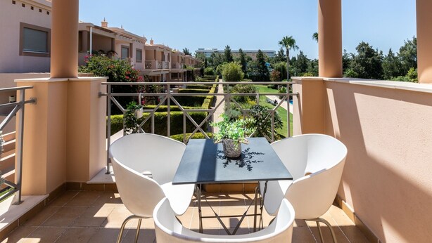 A balcony with a table and two chairs, overlooking a landscaped garden and buildings in the background. - Hali Red Villa, Olhos de Água, Algarve (Albufeira)