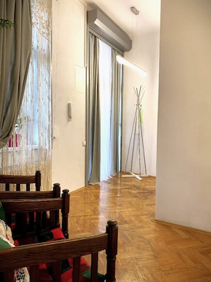 A room with wooden flooring, a wooden chair, a table, and a window with curtains. - Green House apartment (Kraków)