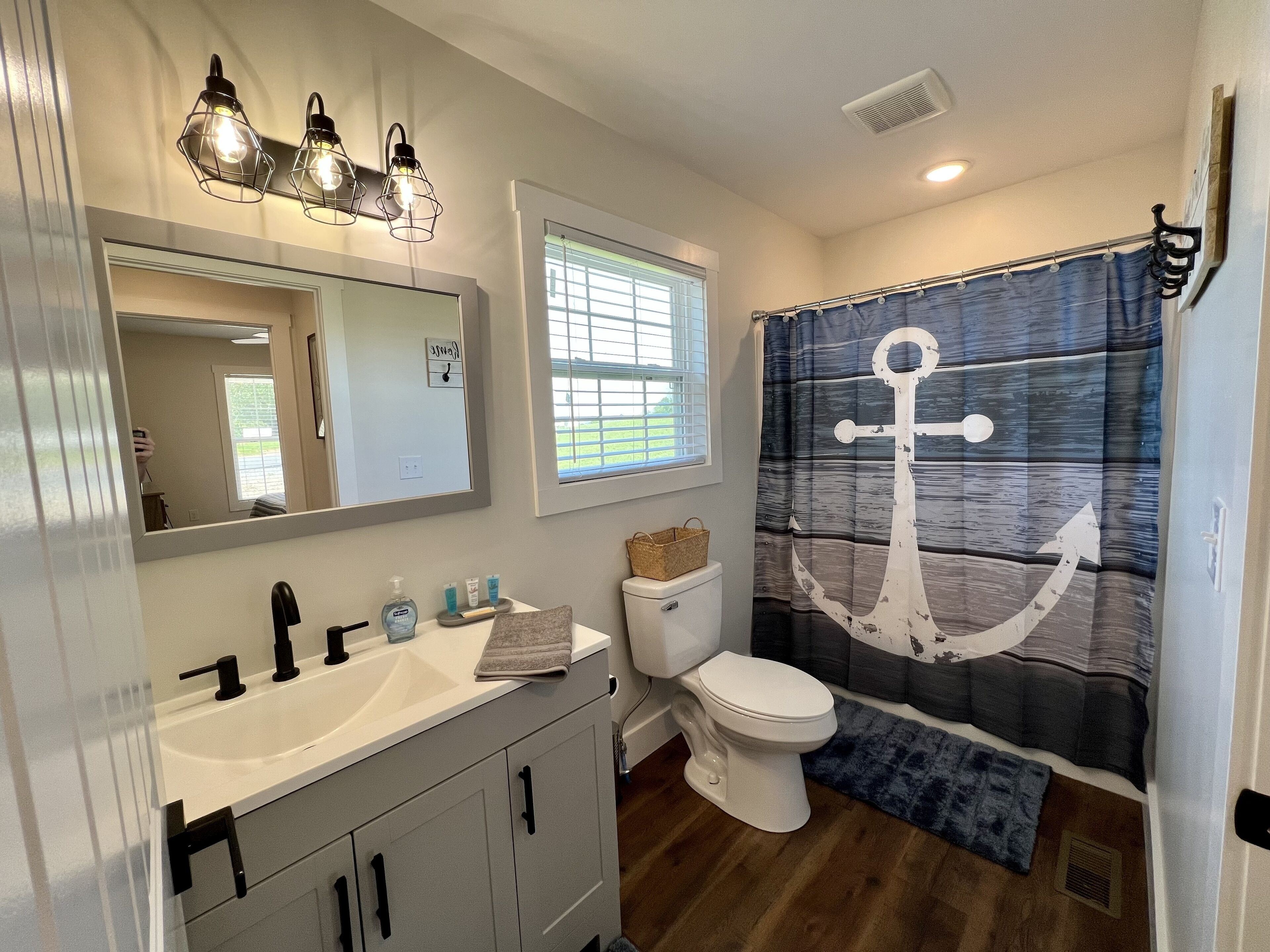 A bathroom with a white sink, a toilet, a mirror, and a shower curtain with an anchor design.