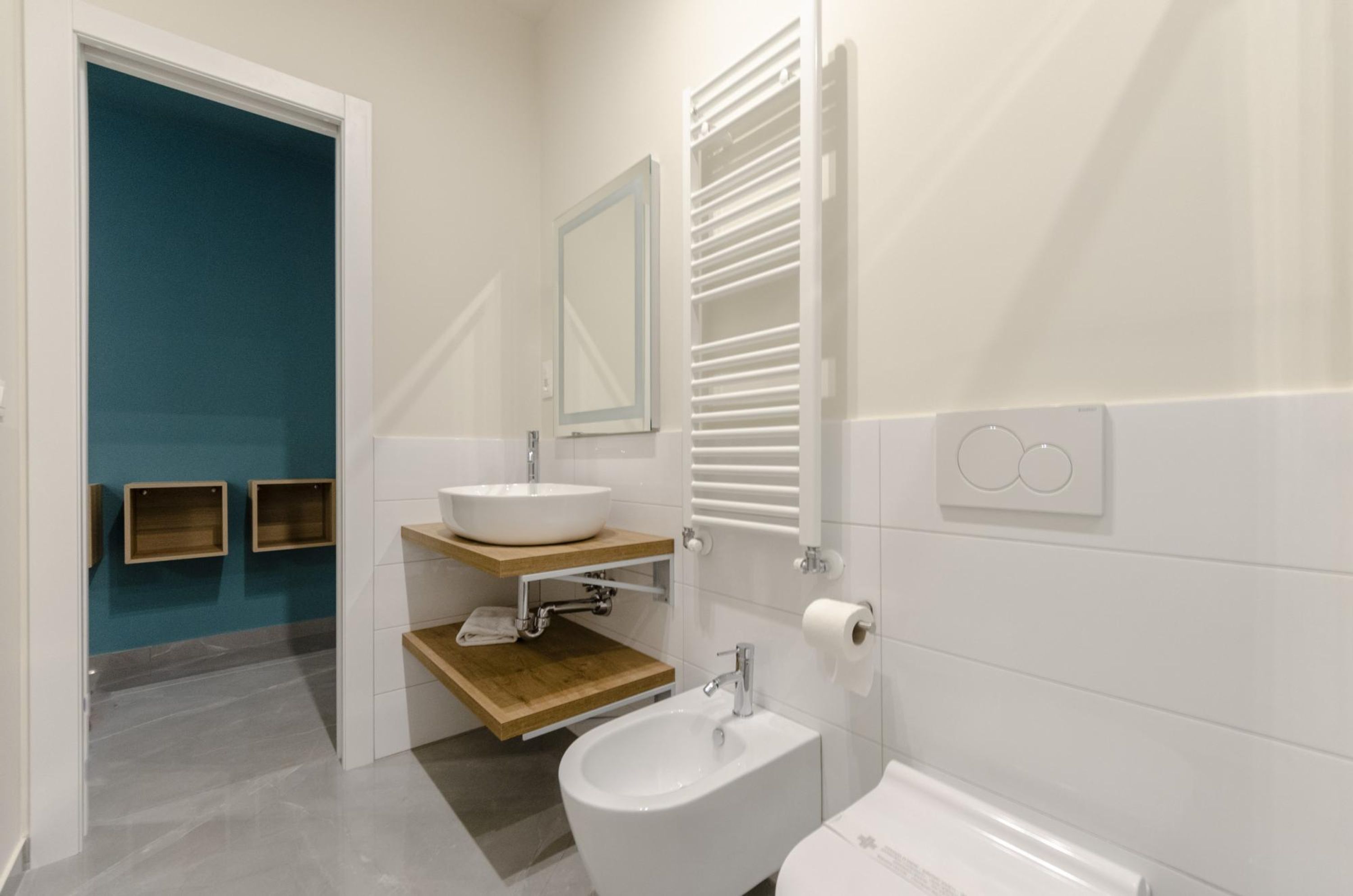 Un baño moderno con un lavamanos blanco, un espejo, un perchero para toallas y un inodoro.