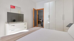 Um quarto com uma cama, uma televisão sobre uma cômoda e um guarda-roupa.