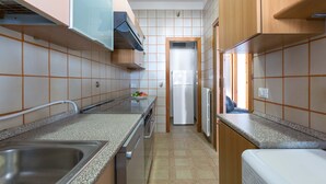 Cozinha estreita com uma pia de aço inoxidável, forno embutido e geladeira.
