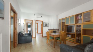 Uma sala de estar com sofá, mesa de jantar com cadeiras, estante de livros e televisão.