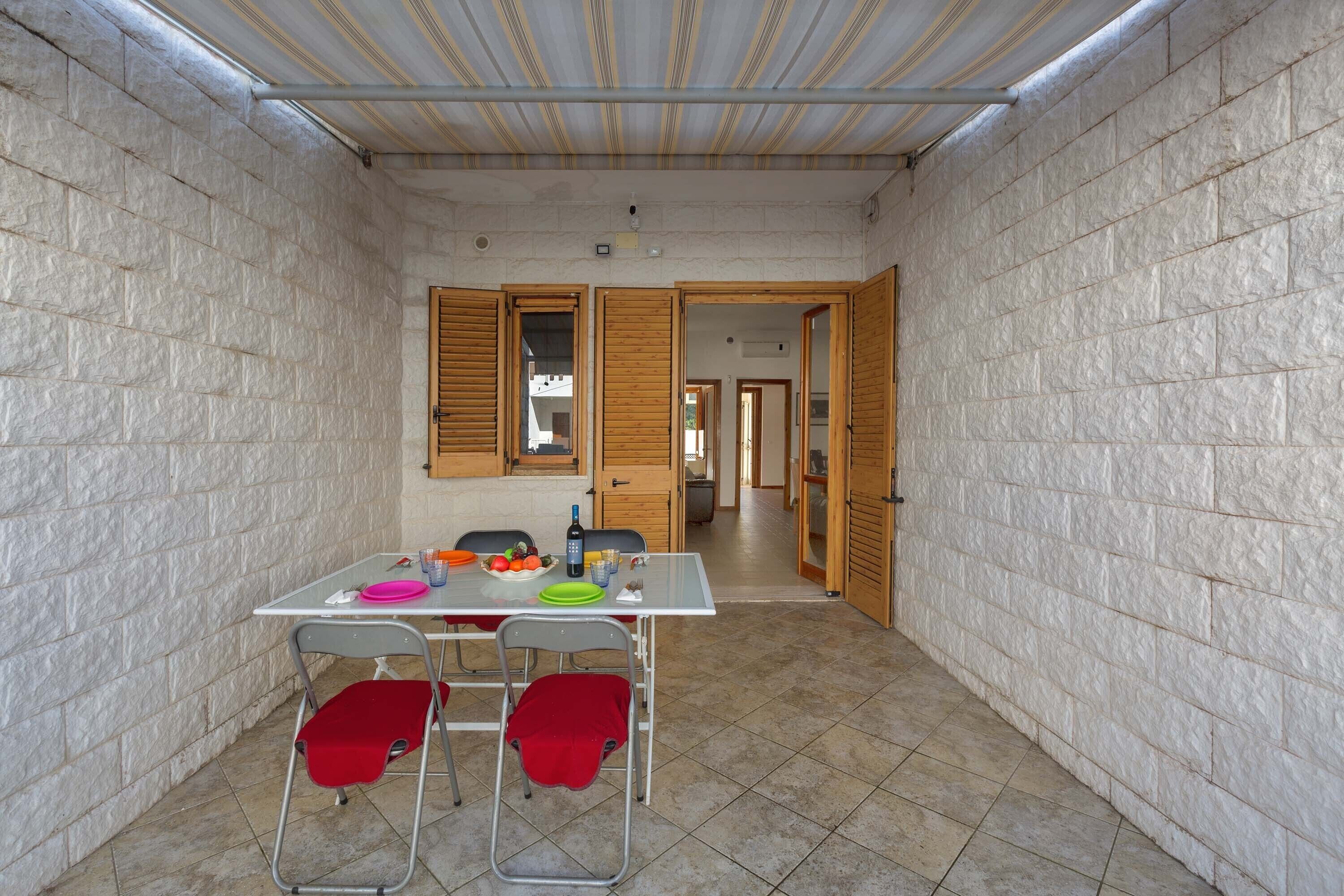 Pequeña habitación con piso de baldosas, una mesa con sillas y una ventana con contraventanas de madera.