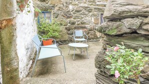 A stone-walled courtyard with two metal chairs and a table, surrounded by potted plants and a small tree.