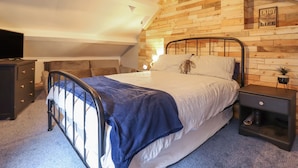 A bedroom with a sloped ceiling, a bed with a headboard, a dresser, a nightstand, and a wall-mounted TV.