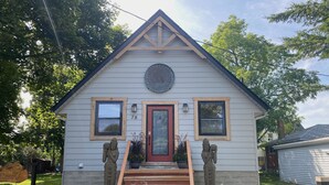 A two-story house with a red door, two windows with wooden frames, and a small porch with steps leading to the front door. - Elora Spa & Residences (Centre Wellington)