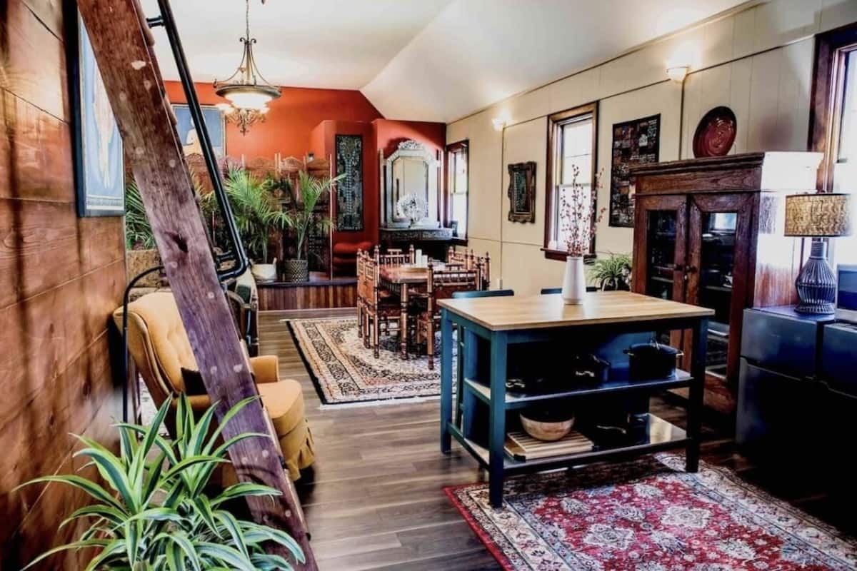 Una sala de estar acogedora con piso de madera, un comedor con mesa y sillas, y un espejo grande en la pared.